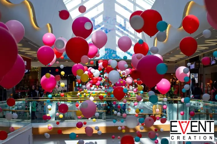 A large shopping mall, is decorated with hundreds of loose balloons in various shades.