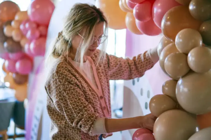 Woman decorating a white arch with peach and pink balloon garland.