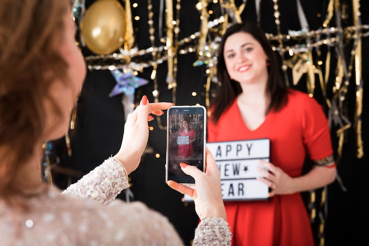 Party planner poses with a 'Happy New Year' sign while a colleague takes her photo at an event.